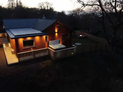 a small house with a porch with lights on it at Hot tub lodge with stunning view in Taynuilt