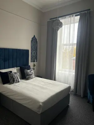 a bedroom with a bed with a blue headboard and a window at Hotel Baba in Uddingston