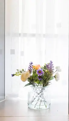 a glass vase filled with flowers in front of a window at 1 BDR Apartment By Caledonia Luxe Stays Short Lets & Serviced Accommodation in Dumbarton