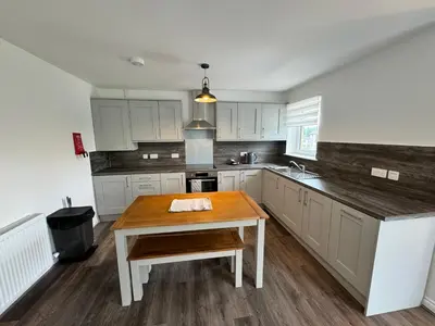 a kitchen with white cabinets and a wooden table at Inchfad Apartment 2/1 in Bonhill