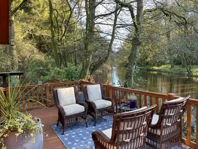 three chairs and a table on a deck next to a river at Riverbank Lodge in Dollar