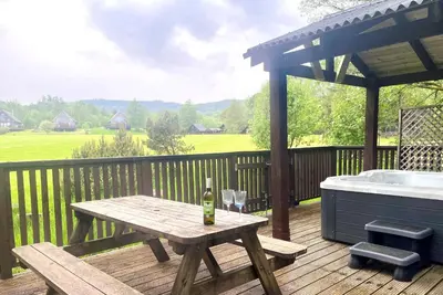a picnic table with a bottle of wine on a deck at Rowan Log Cabin in Dalavich