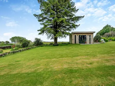 a tree in the middle of a field with a building at Carraig Dhubh Cottage - Uk47123 in Whiting Bay