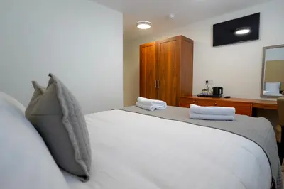 a bedroom with a white bed and a wooden cabinet at Hardgate House Hotel in Clydebank