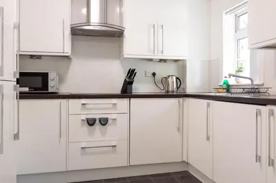 a white kitchen with white cabinets and a sink at Croftspar House in Glasgow