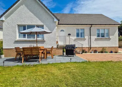 a table and chairs with an umbrella in front of a house at Kilin in Lochgilphead