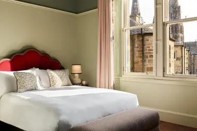 a bedroom with a large bed with a red headboard and a window at The Hoxton, Edinburgh in Edinburgh