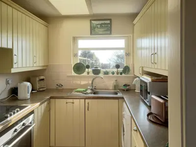 a kitchen with white cabinets and a sink and a window at Tarandoun Cottage in Helensburgh