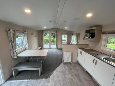 a kitchen with white cabinets and a table in a caravan at Newton Stewart - Lodge - Sleeps 4 - Garden in Bargrennan