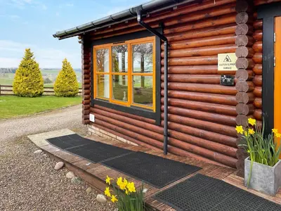 a log cabin with a window and some flowers at Ashknowe Log Cabin - S4590 in Glenfarg