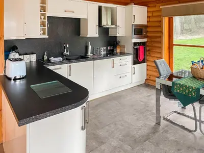 a kitchen with white cabinets and a black counter top at Ashknowe Log Cabin - S4590 in Glenfarg