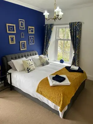 a bedroom with a large bed with blue walls at Clarefoot Cottage in Moffat