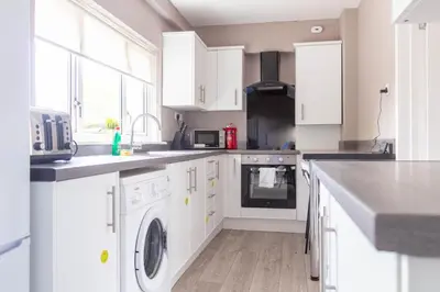 a kitchen with white cabinets and a washer and dryer at Campsie View in Glasgow