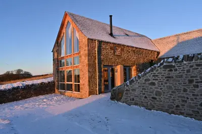 a brick building in the snow next to a wall at Falcon Steading in Buchanty