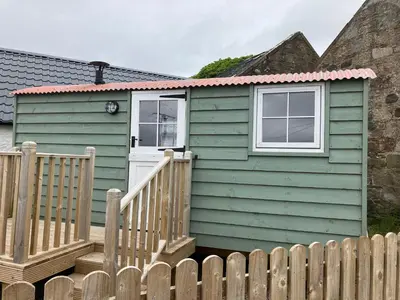 a green house with a white door and a fence at Wee Beach Hut Maidens in Maidens