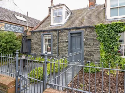 a stone house with a fence in front of it at Wee Cottage in Moffat