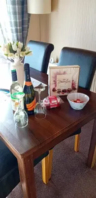 a wooden table with two bottles and a box of wine at Baytree Lodge at three lochs holiday park, NEW ASK ABOUT OUR PACKAGES birthday ,anniversary,family,pamper packages available in Balminnoch