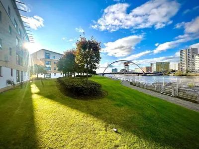 a green park next to a river with a bridge at Cosy Riverside Home SECC Hydro in Glasgow
