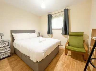 a bedroom with a bed and a green chair at Cosy Riverside Home SECC Hydro in Glasgow