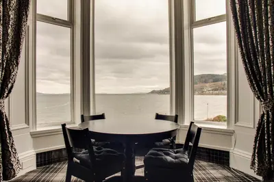 a table and chairs in a room with windows at St Ives Boutique Hotel in Dunoon