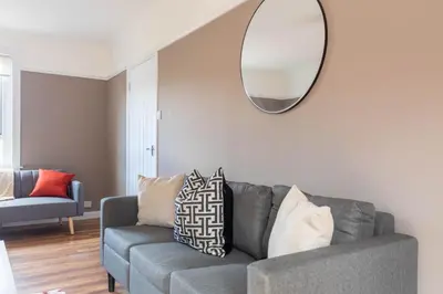 a living room with a gray couch and a mirror at Beth House in Bathgate