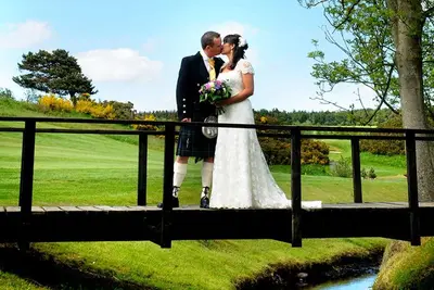 a bride and groom kissing on a bridge at Forrester Park Resort in Dunfermline
