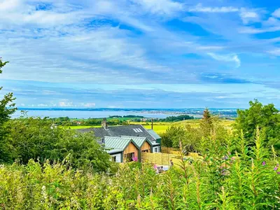 a house sitting on top of a hill with trees at Firth View 1 - Luxury Cottage with Sea View & Hot Tub, Ayr in Ayr