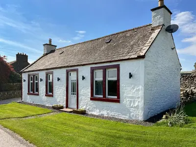 a white cottage with red windows and a grass yard at Kilquhanity Cottage in Castle Douglas