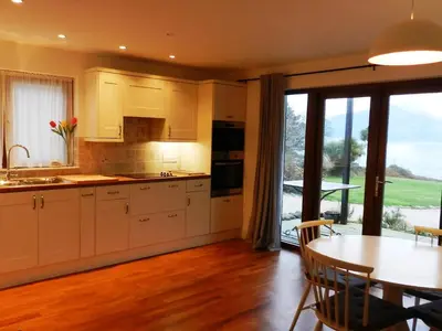 a kitchen with white cabinets and a table and a dining room at Seaview Cottage in Lamlash