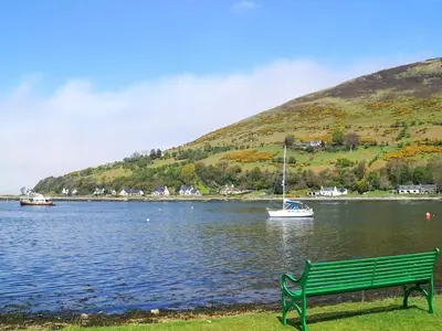 a green bench sitting next to a lake with a boat at Seaview Cottage in Lamlash