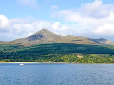 a boat on a lake with a mountain in the background at Seaview Cottage in Lamlash