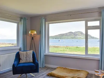 a living room with two large windows and a blue chair at Kinneil Land in Lamlash