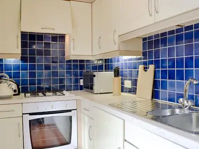 a kitchen with white cabinets and blue tiles on the wall at Brough Hall in Paisley