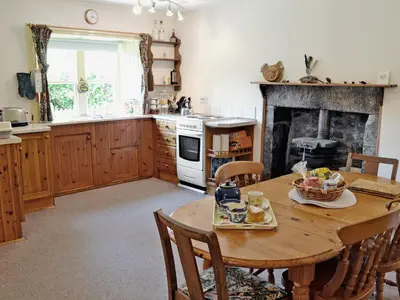 a kitchen with a wooden table and chairs and a fireplace at Squirrel Cottage in Palnure