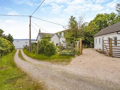 a gravel road next to a house and a fence at Sea Breeze Cottage in Lochranza