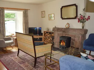 a living room with a fireplace and a chair at Old Steading in Brodick