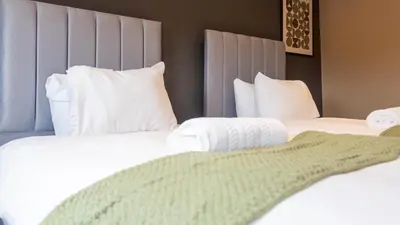 two beds in a hotel room with white sheets and pillows at Moncrieff House in Livingston