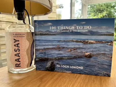 a bottle of alcohol next to a book on a table at House in Drymen Village with free local health club access in Glasgow