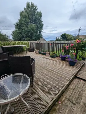a wooden deck with a table and chairs and flowers at Single room with beautiful garden in Edinburgh