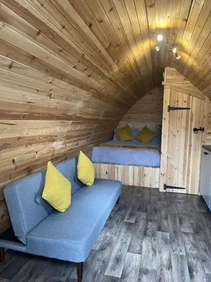 a blue couch with yellow pillows in a wooden room at Penny gown farm pod in Campbeltown