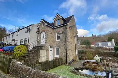 an old stone house with a pond in front of it at Loch Lomond 2 Bedroom Apartment in Tarbet