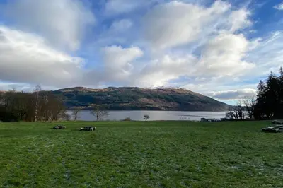 a field with a lake and mountains in the background at Loch Lomond 2 Bedroom Apartment in Tarbet
