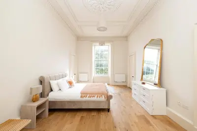 a white bedroom with a bed and a mirror at JOIVY Exclusive house with free parking in Edinburgh
