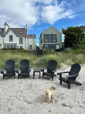 a dog sitting in the sand in front of chairs and a house at Unique house in an idyllic situation on a beach in Port Ellen