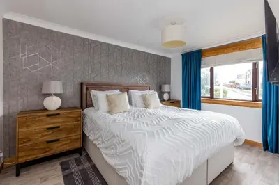 a bedroom with a bed with blue curtains and a window at 20 mins to Edinburgh 3 bedroom detached family house Wi-Fi Parking in Fife
