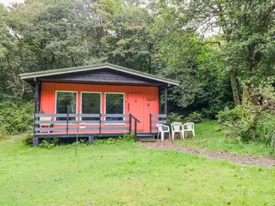 a small red cabin with two chairs in the grass at Lodge 1 