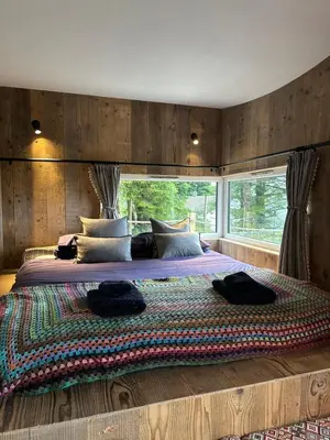 a bedroom with a large bed with a large window at Otter Burn Cabin in Oban