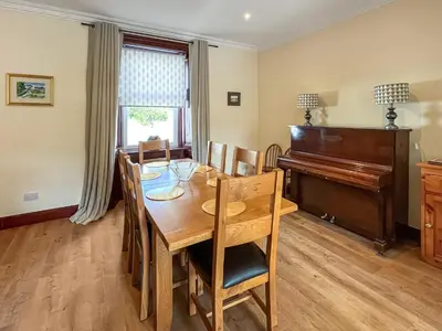 a dining room with a table and a piano at Arden in Glenluce