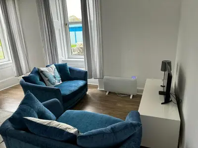 a living room with two blue chairs and a table at Our Wee Eden - Rothesay in Rothesay