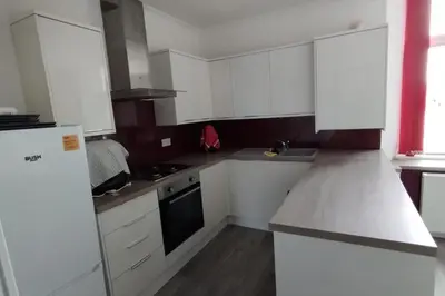 a small kitchen with white cabinets and a refrigerator at Lovely flat near Glasgow in Barrhead